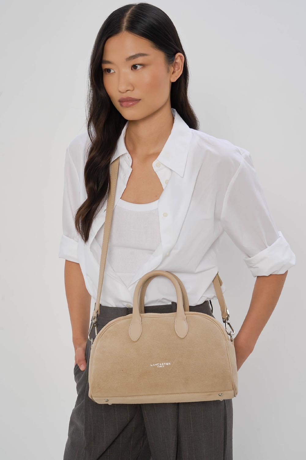 Lancaster, beige Bowlingtasche in der Hand getragen, zu weißem Hemd und grauer Hose.