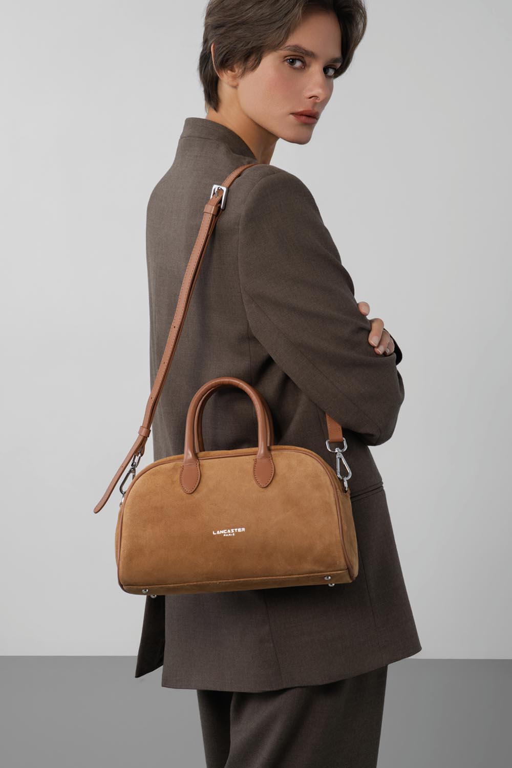 Lancaster, braune Bowlingtasche quer über dem Körper getragen zu braunem Hosenanzug und schwarzem Oberteil.