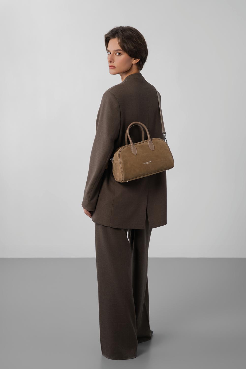 Lancaster, braune Bowlingtasche, in der Hand getragen zu braunem Blazer und Hose.