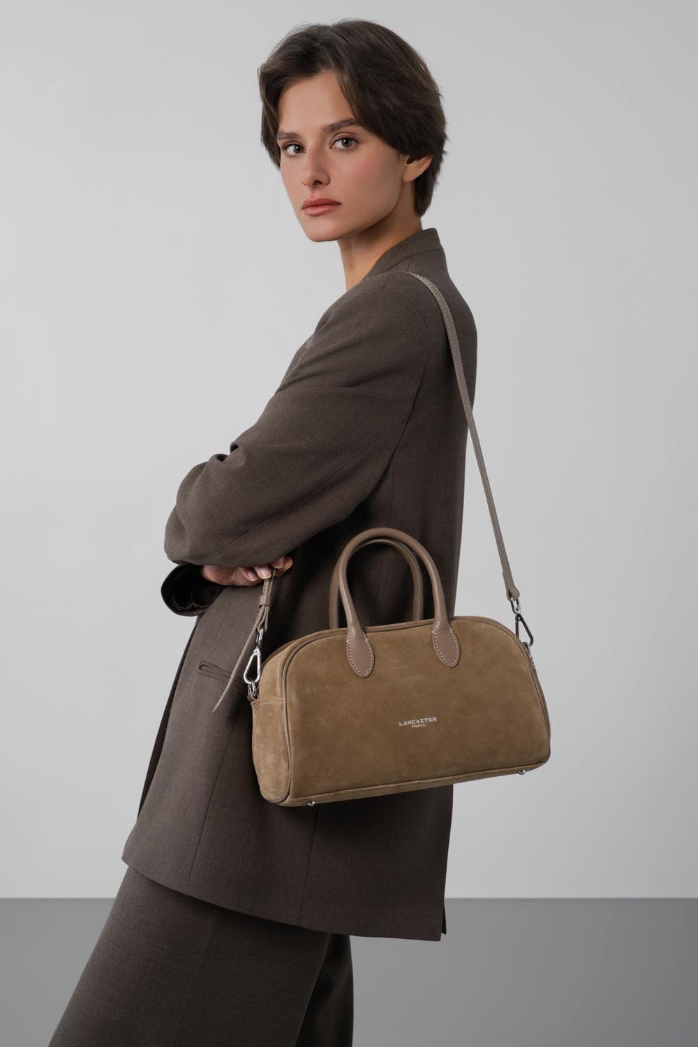 Lancaster, brown bowling bag worn over the shoulder with a blazer and matching trousers.