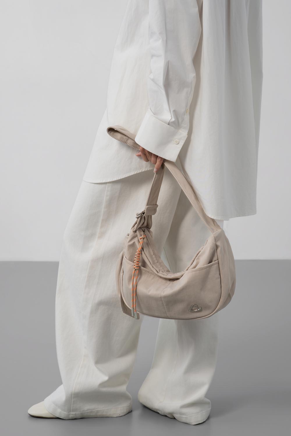 Lancaster Basic Love Praline Messenger Bag – Held by hand, the beige Basic shoulder bag completes an outfit of a long shirt and white trousers.
