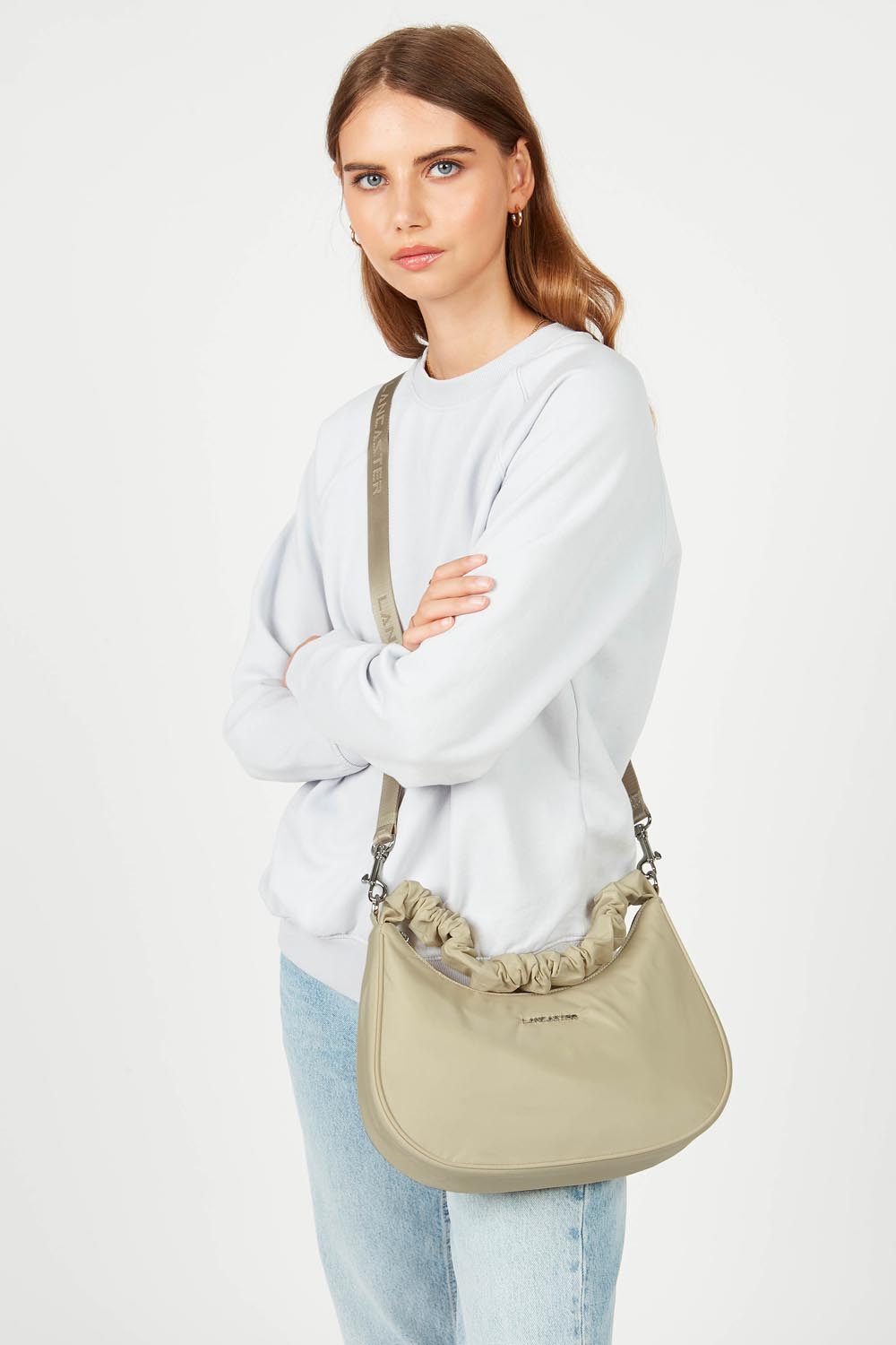 Mala hobo Lancaster Basic Chouchou bege, usada a tiracolo com uma camisola branca e calças de ganga azul-claro.