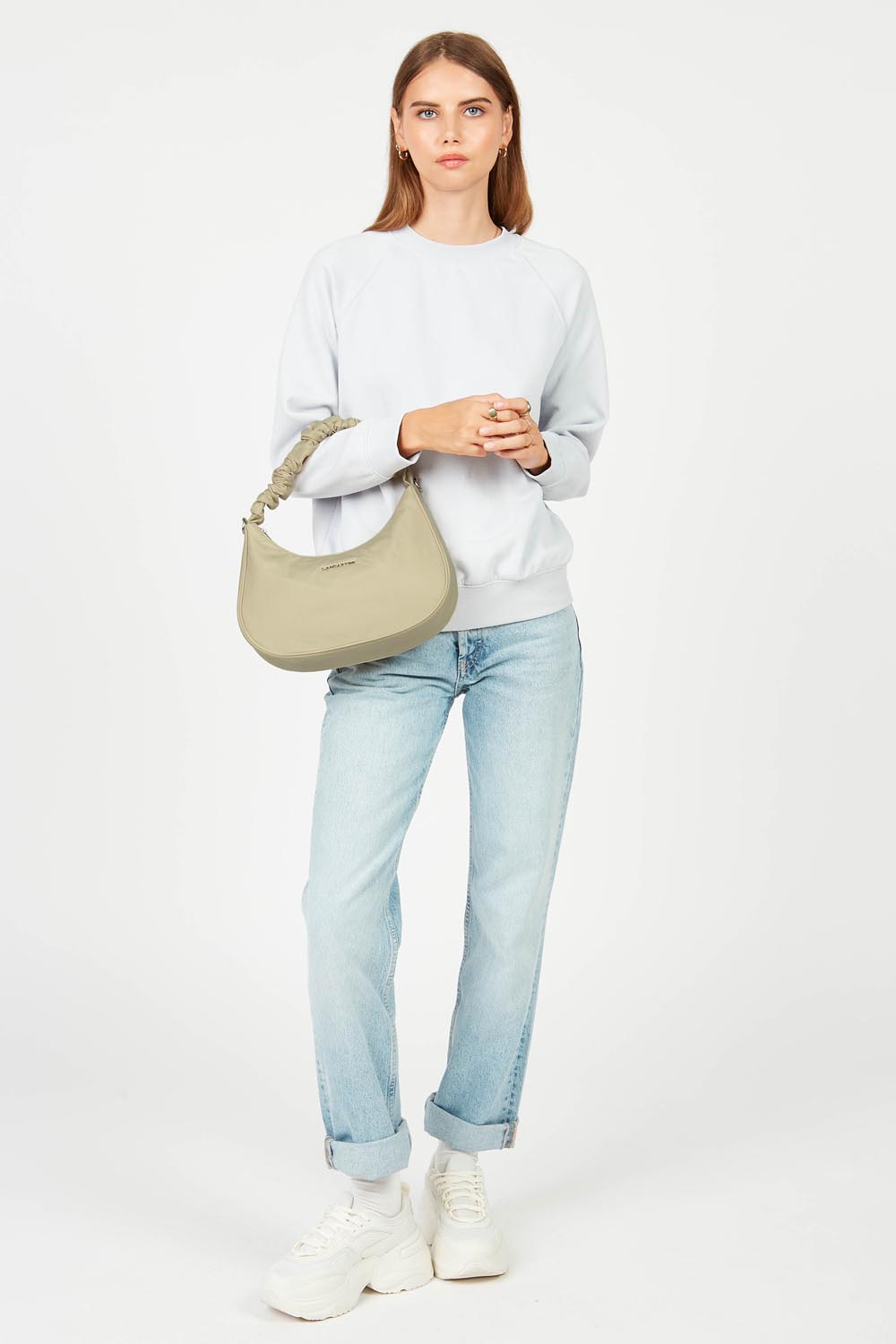 Lancaster, mala hobo Basic Chouchou bege ao ombro, com camisola branca e jeans azul-claros.