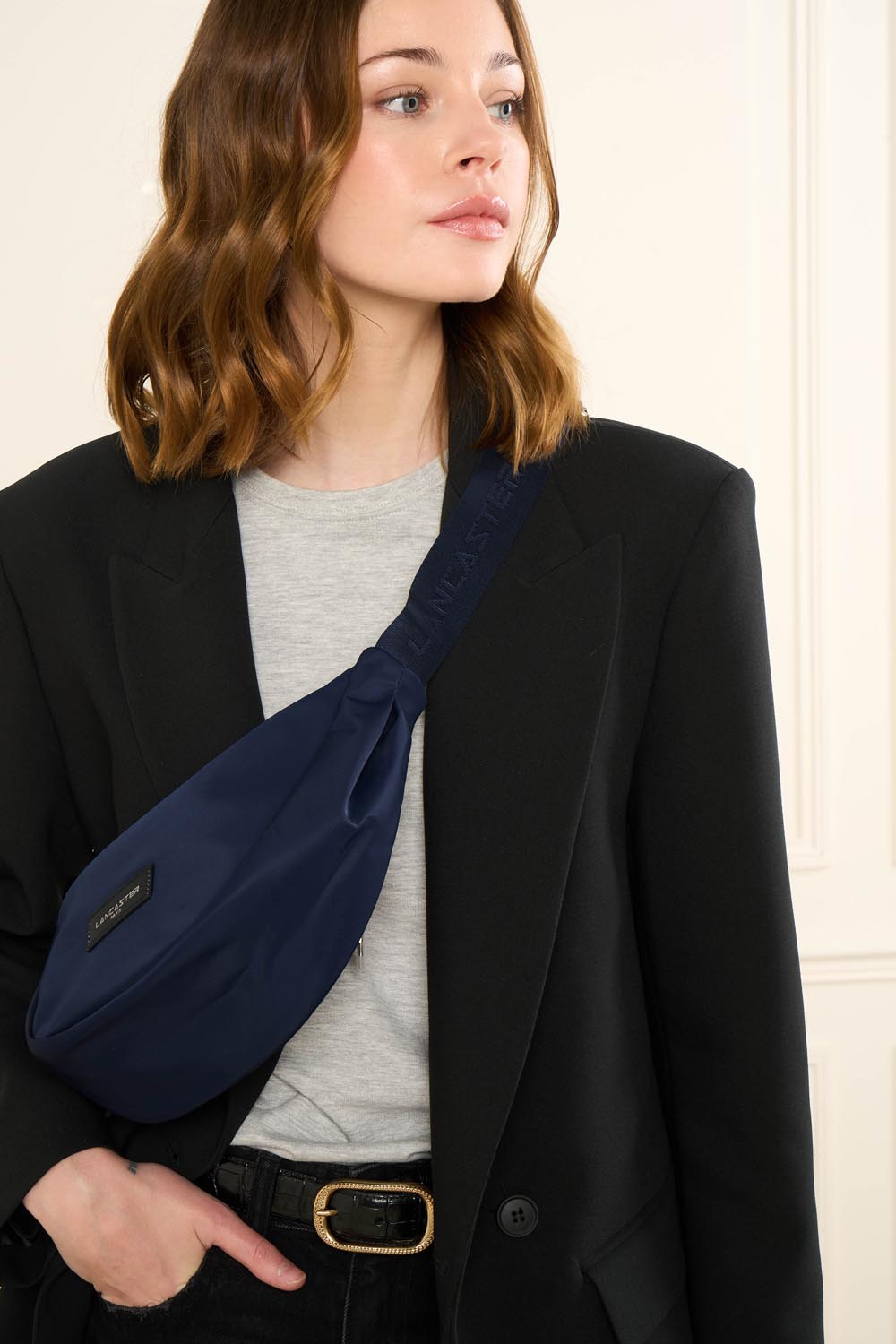 Sac banane Zippé Basic Vita Lancaster Gris Clair – Schwaarze Blazer a groechen Top fir déi blo Basic Vita-Banannentäsch, queesch iwwer de Kierper gedroen.