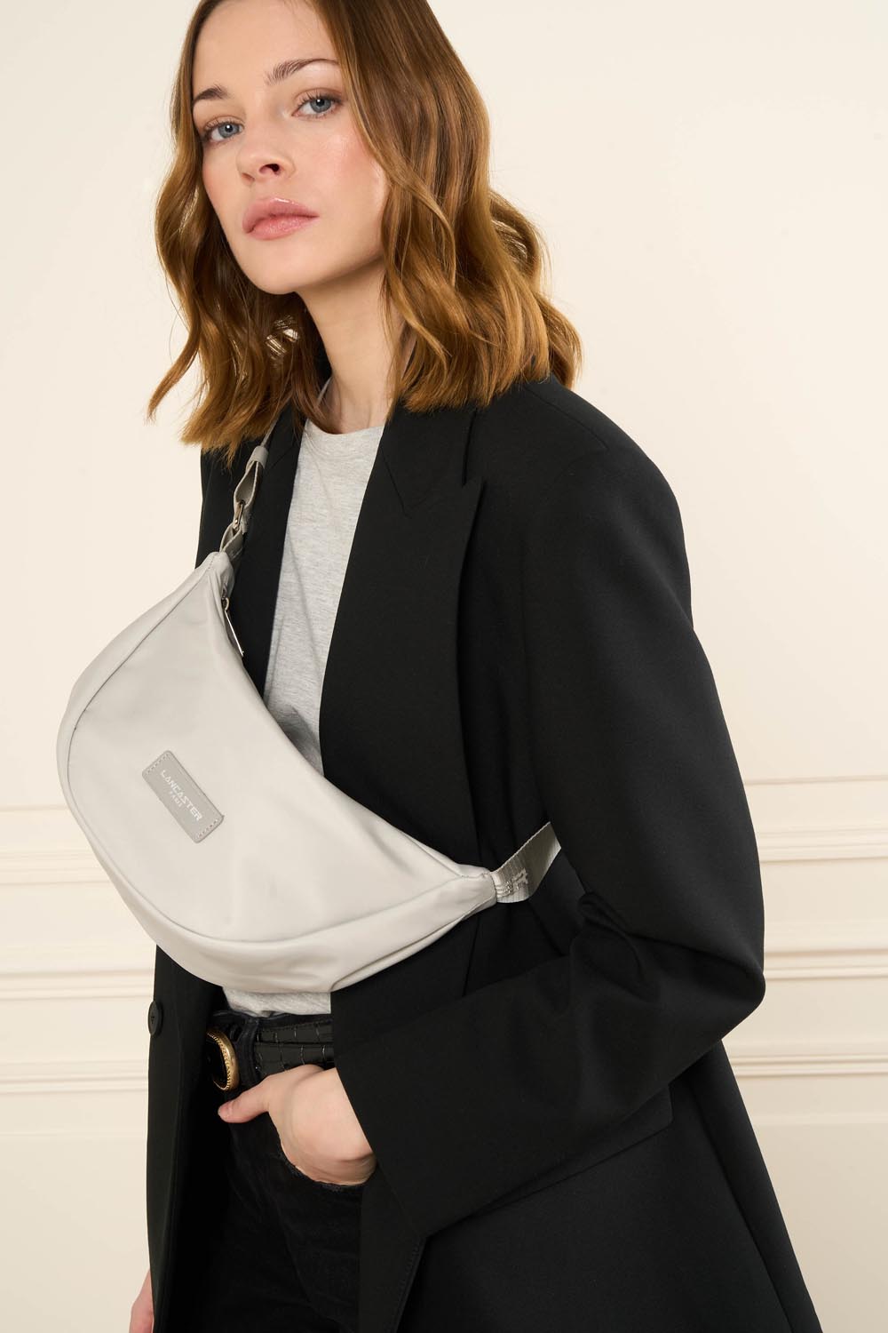 Sac banane Zippé Basic Vita Lancaster Gris Clair – Déi gro Banannentasch Basic Vita gëtt queesch iwwer engem schwaarze Blazer an engem hellgroen Top gedroen.