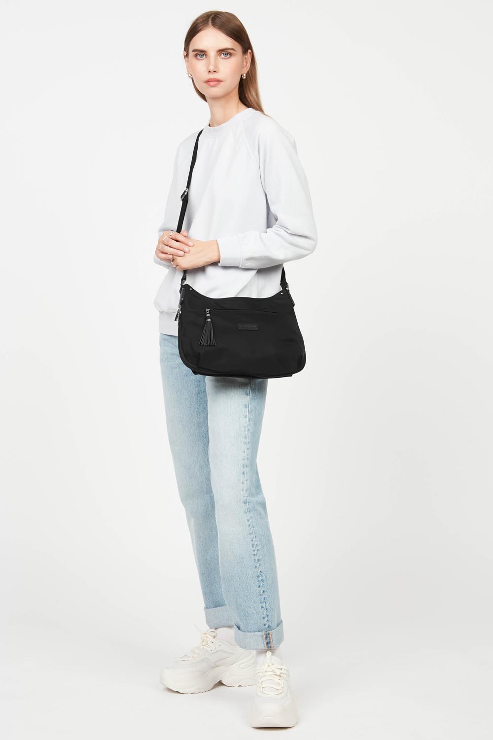 Lancaster Sac besace basic Pompon – La besace Basic Pompon se porte en bandoulière avec un haut blanc et un jean bleu clair.