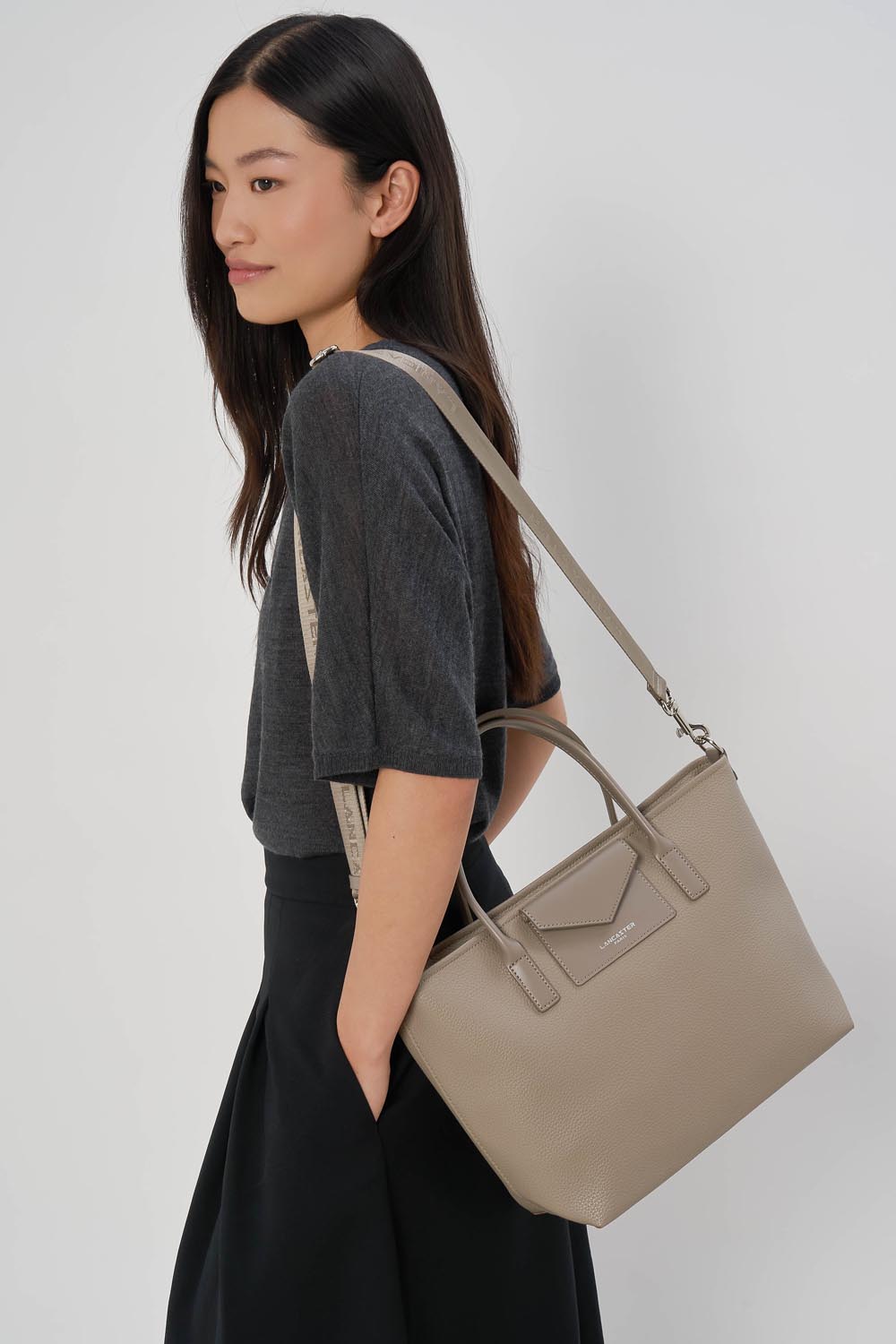 Saco Cabaz de Mão Lancaster Maya Double Kba Pele Bege Escuro – O saco shopper Maya Double KBA está ao ombro e combina com um top cinzento e uma saia preta.