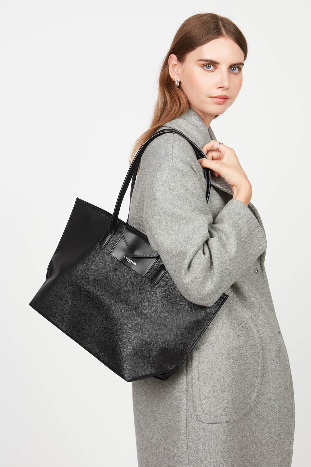 Lancaster Schultertasche Zippée L Maya – Der Shopper Maya wird über der Schulter zu einem grauen Mantel getragen.