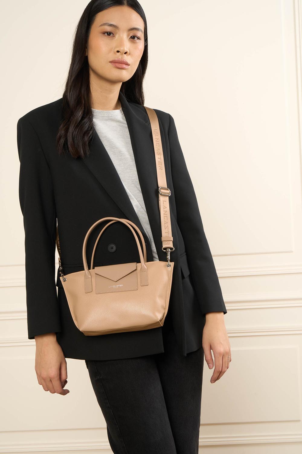 Lancaster Maya KBA gold mini bag, worn crossbody with a black blazer, white top and black trousers.