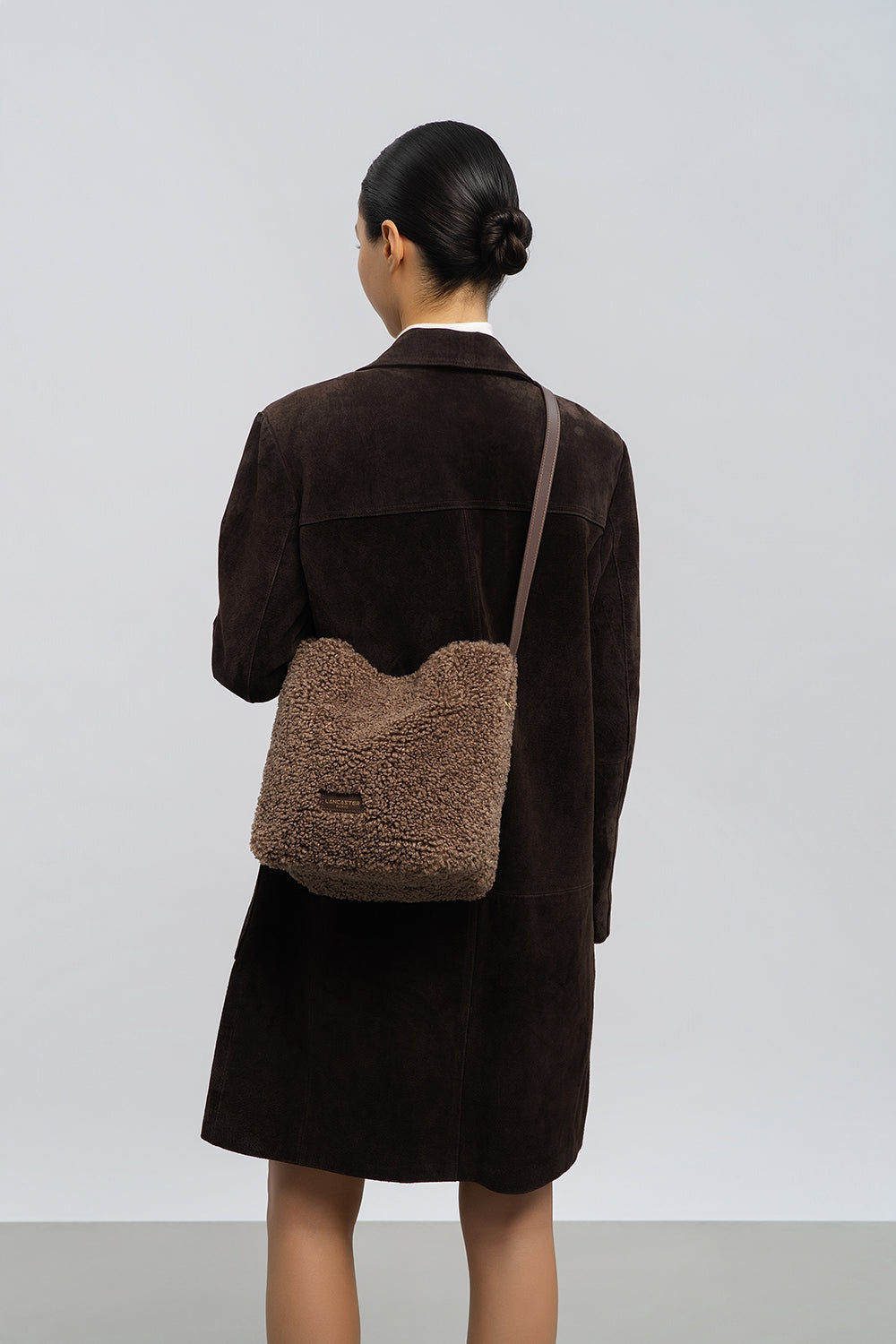 Lancaster Bucket Bag Magnetic Moumoute Ecru - Black – The brown Moumoute bucket bag is worn crossbody with a black coat.