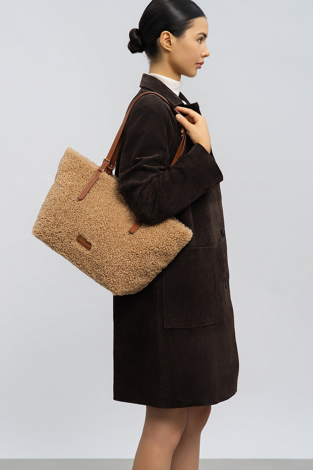 Lancaster, cabas Moumoute marron porté à l’épaule avec un manteau marron et une jupe noire.