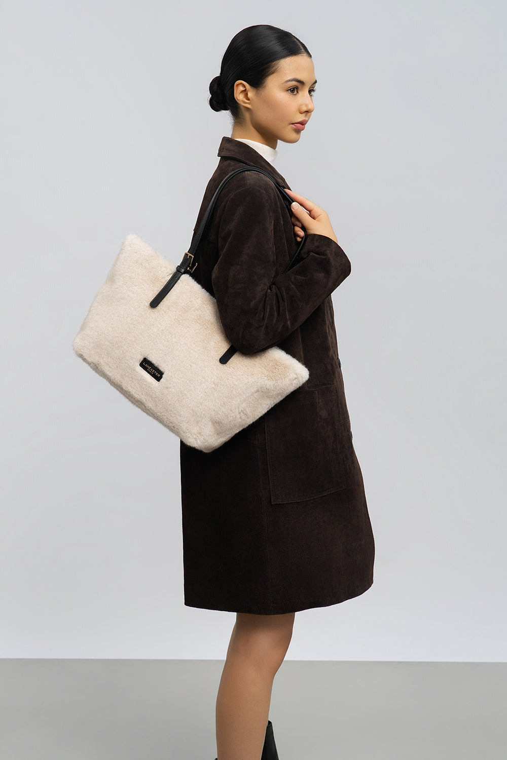 Lancaster, cabas Moumoute beige porté à l’épaule avec un manteau brun.