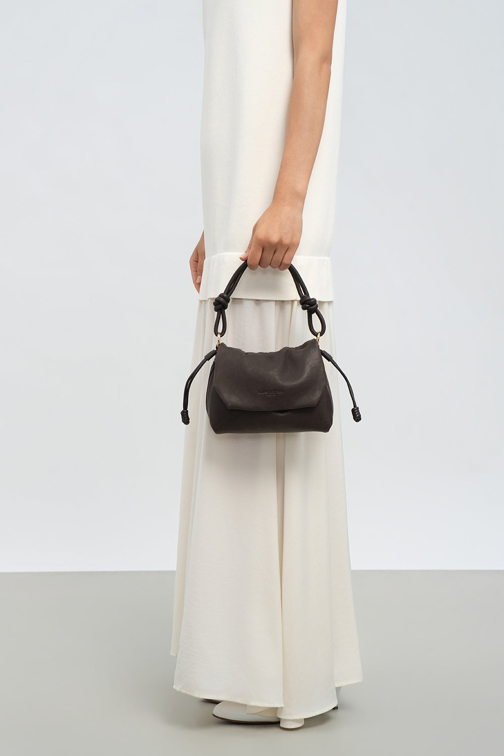 Lancaster Borsa a tracolla con patta magnetica S Lush Nero – La borsa a tracolla Lush è tenuta a mano davanti a un lungo abito bianco.