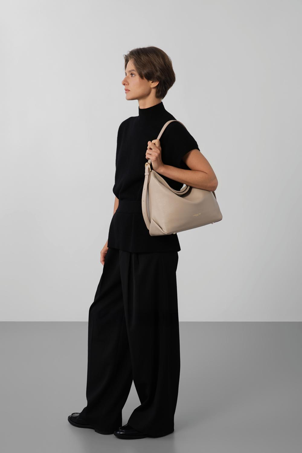 Lancaster Borsa a secchiello con zip Dune Blu – Pantaloni neri e top a maniche corte per la borsa a secchiello Dune, portata a spalla.