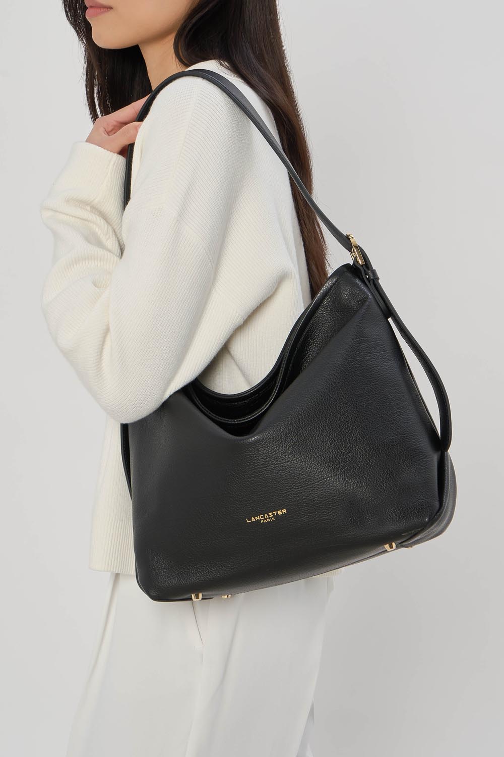 Lancaster Borsa a secchiello con zip Dune Blu – La borsa a secchiello Dune nera si porta a spalla con un maglione bianco e pantaloni bianchi.