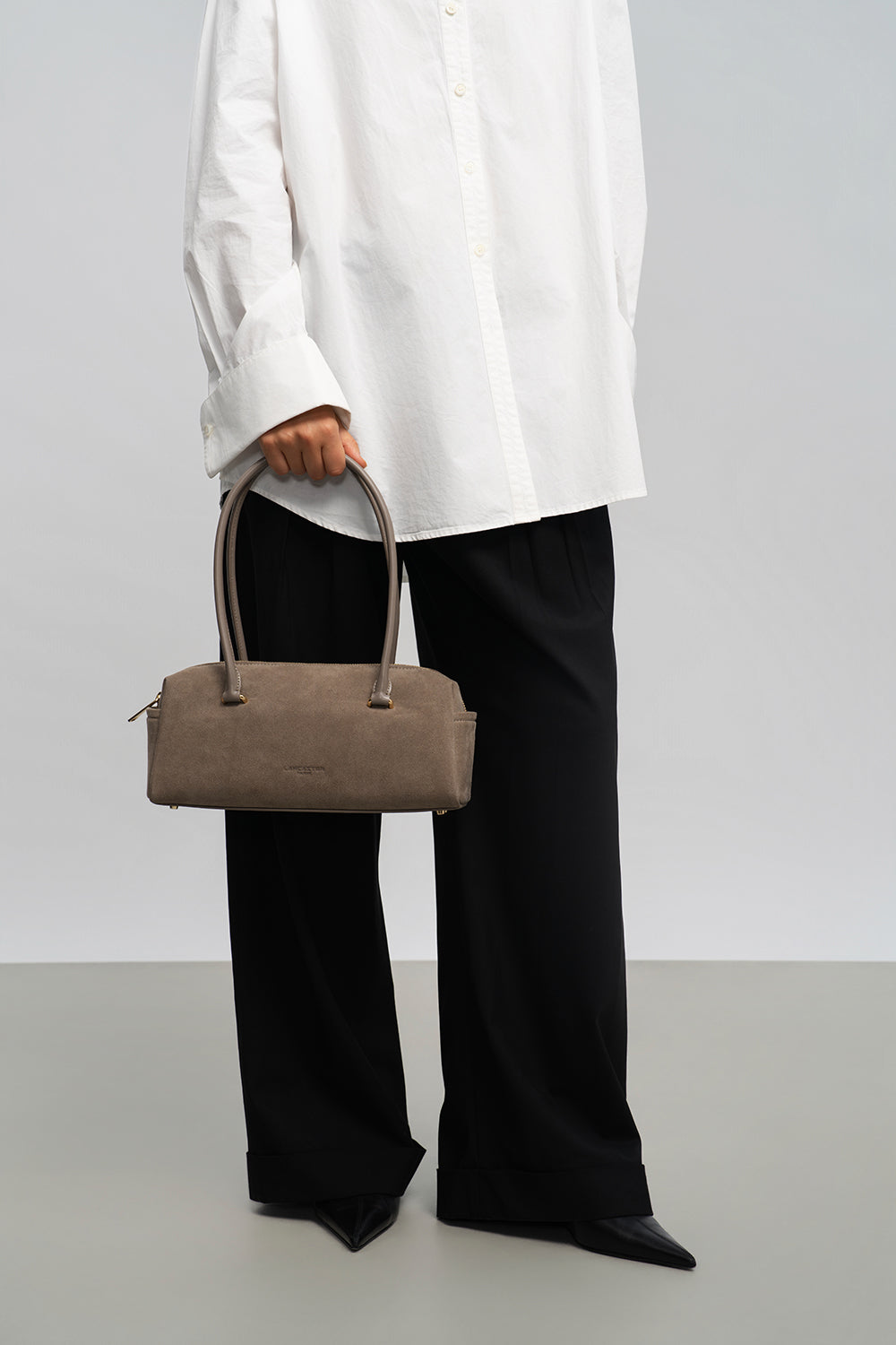 Lancaster Rectangle Bag Zippered Suède Cube Brown – The grey Rectangle bag is held by hand with a white shirt and black trousers.