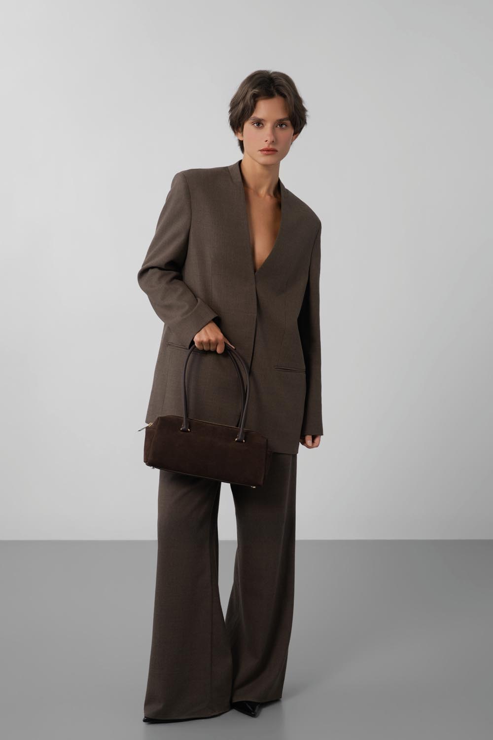 Lancaster Rectangle Bag Zippered Suède Cube Brown – The brown rectangular bag is held by hand with a relaxed brown trouser suit.