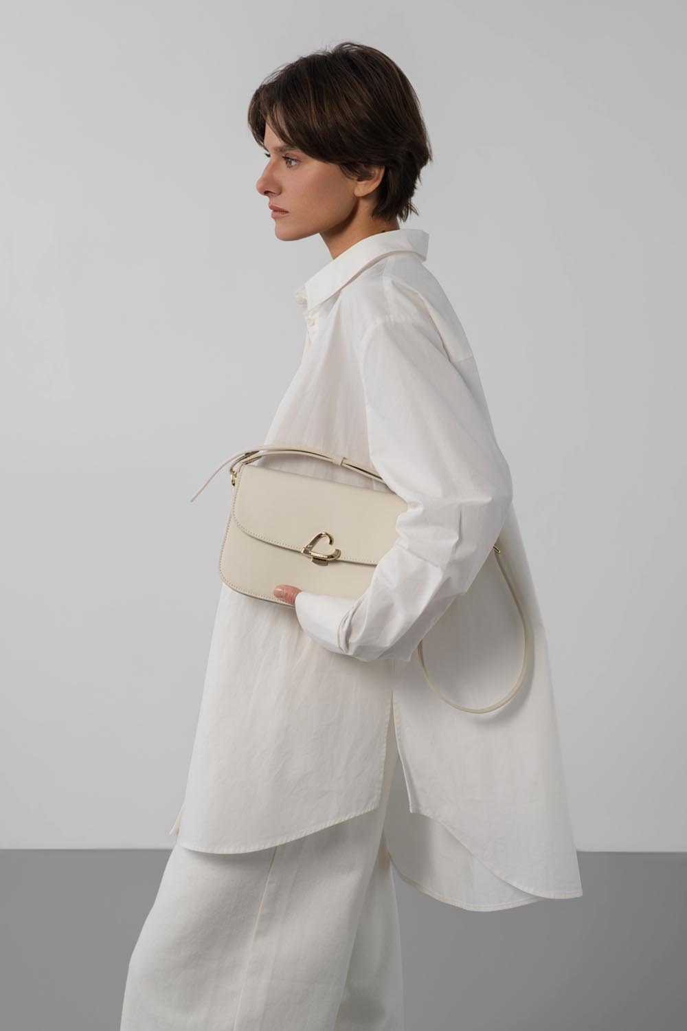 Lancaster Sac trotteur à rabat aimanté Paris Philos Noir – Mat enger wäisser Blouse an enger wäisser Box läit den Trotteur Paris Philos an der Aarmbeug.