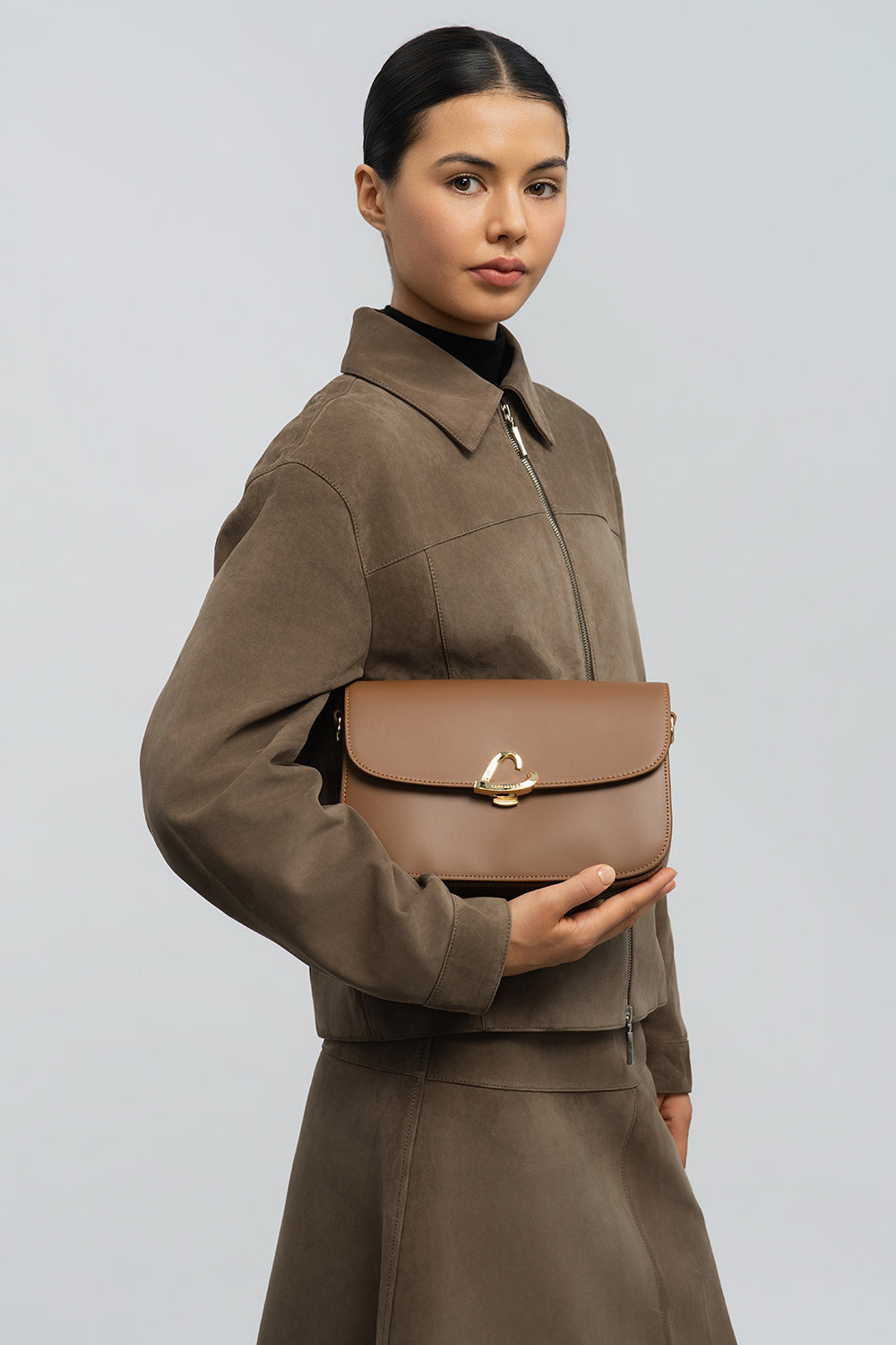Lancaster Sac trotteur à rabat aimanté Paris Philos Noir – Den Trotteur Paris Philos gëtt an der Hand virun enger bronger Jackett an engem bronge Rock gehalen.