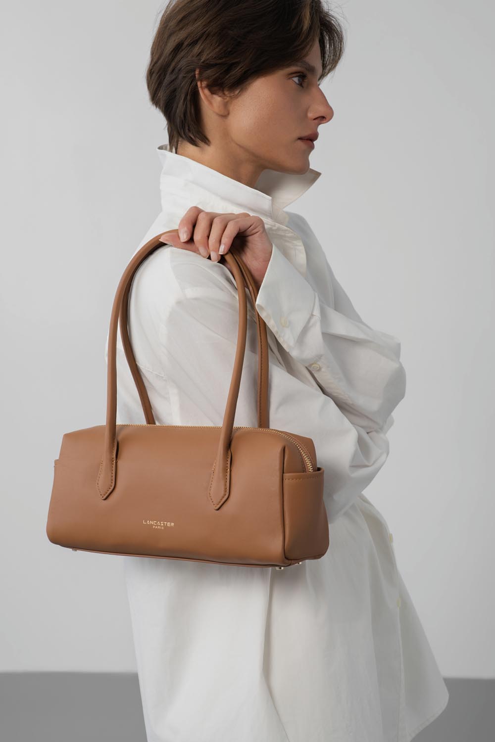 Lancaster Donna Cube Zipped Crossbody Bag Linen – A white shirt and white trousers with the Donna Cube trotter, carried by hand.