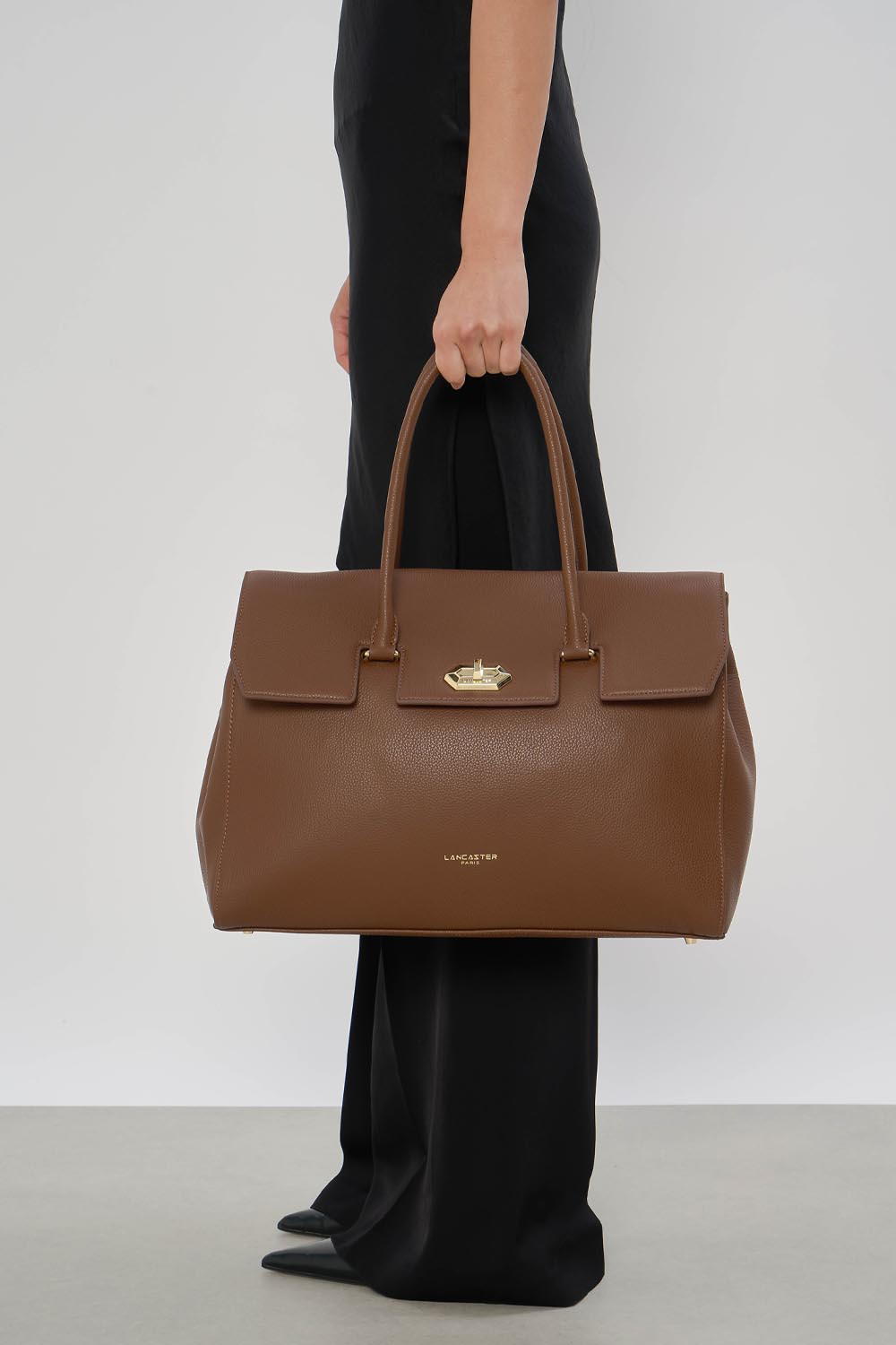 Lancaster Borsa Shopper Foulonné Milano XL Champagne – La borsa shopper marrone è tenuta a mano con pantaloni neri e scarpe nere.