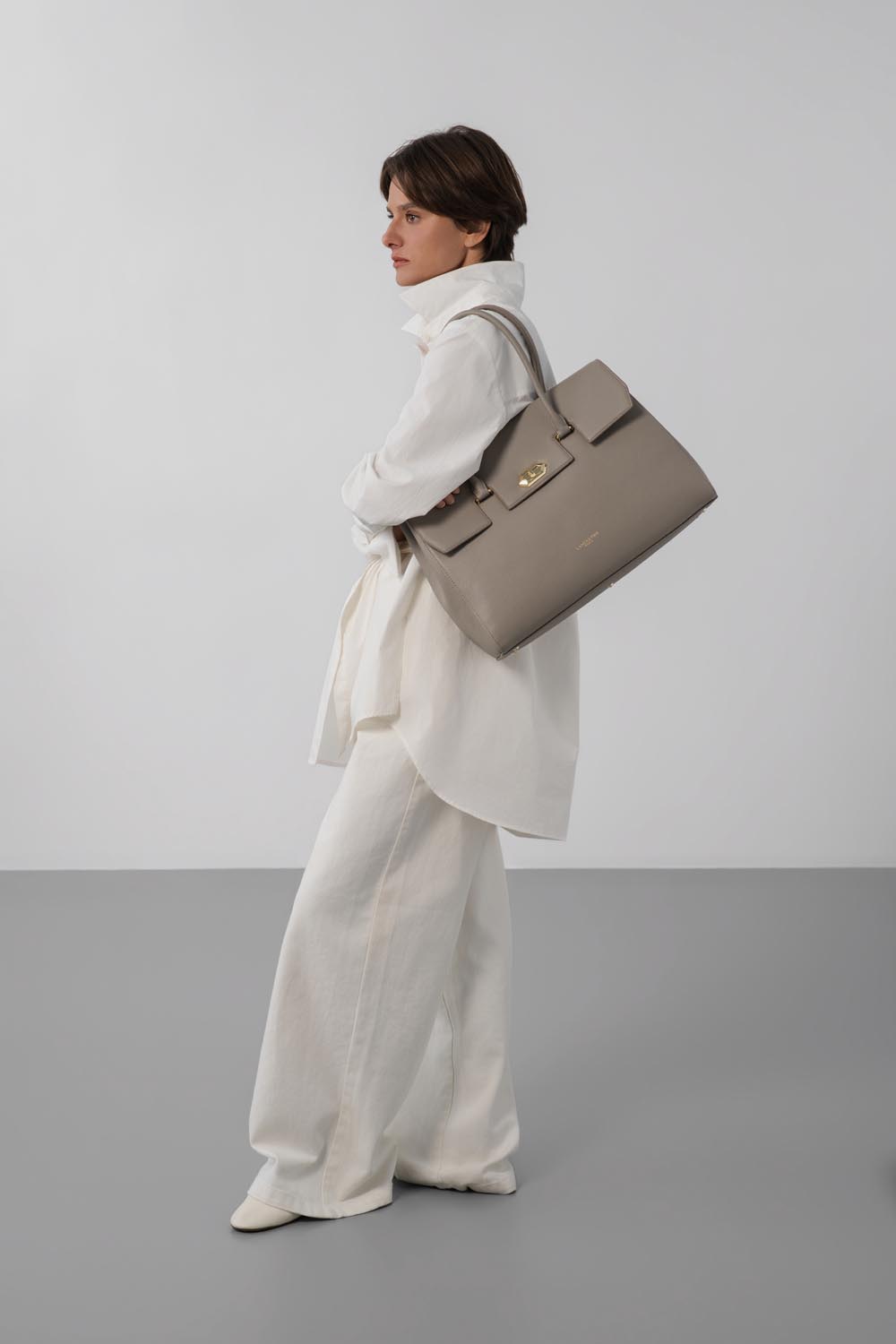 Lancaster Borsa Shopper Foulonné Milano XL Champagne – Portata a spalla, la borsa shopper color tortora si abbina a una camicia bianca e a pantaloni bianchi ampi.