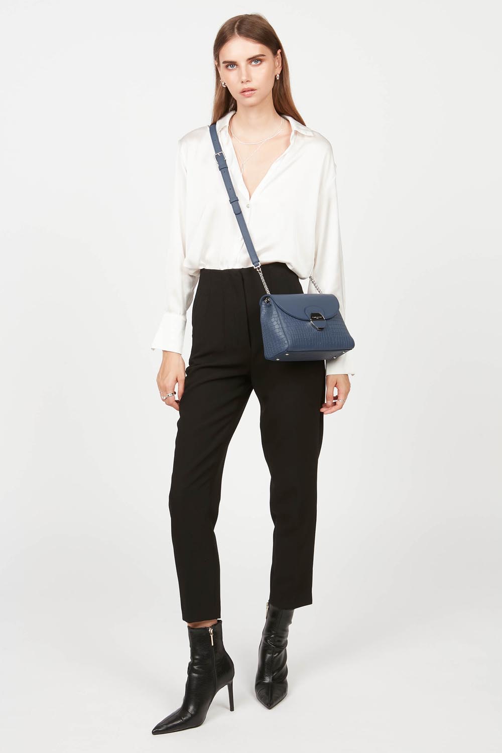Lancaster Pia Camel Flap Crossbody Bag – The Pia satchel is worn crossbody with a white shirt and black trousers.