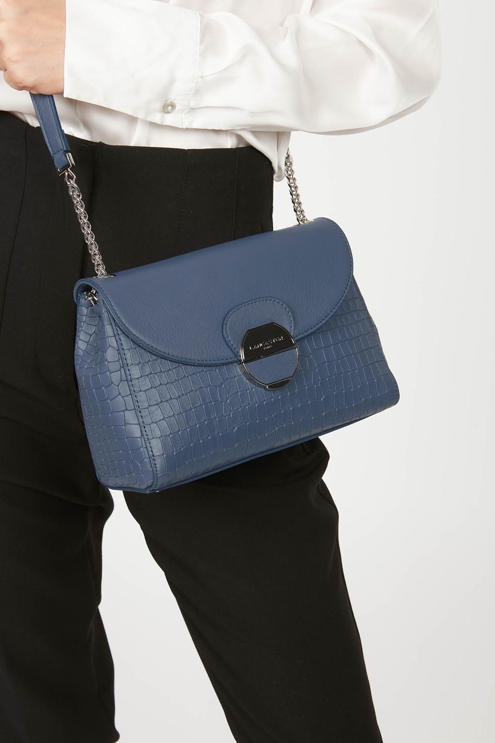 Lancaster Pia Camel Flap Crossbody Bag – A white shirt and black trousers with the Pia trotteur, held in the hand.