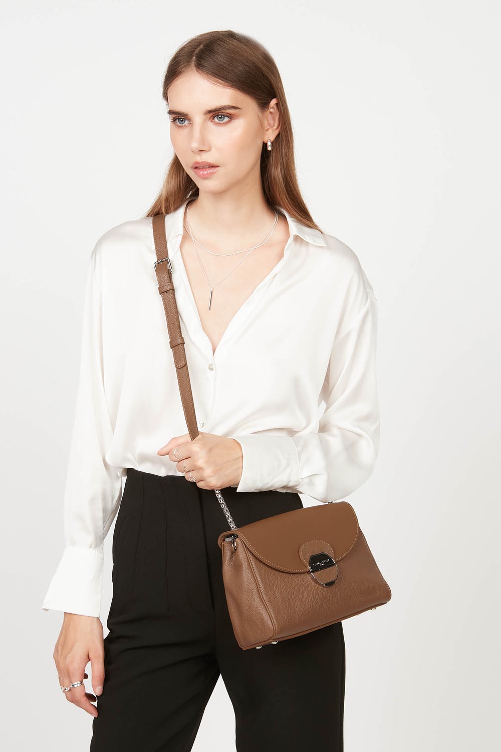 Lancaster Pia Camel Flap Crossbody Bag – Worn crossbody, the brown Pia trotteur pairs with a white blouse and black trousers.