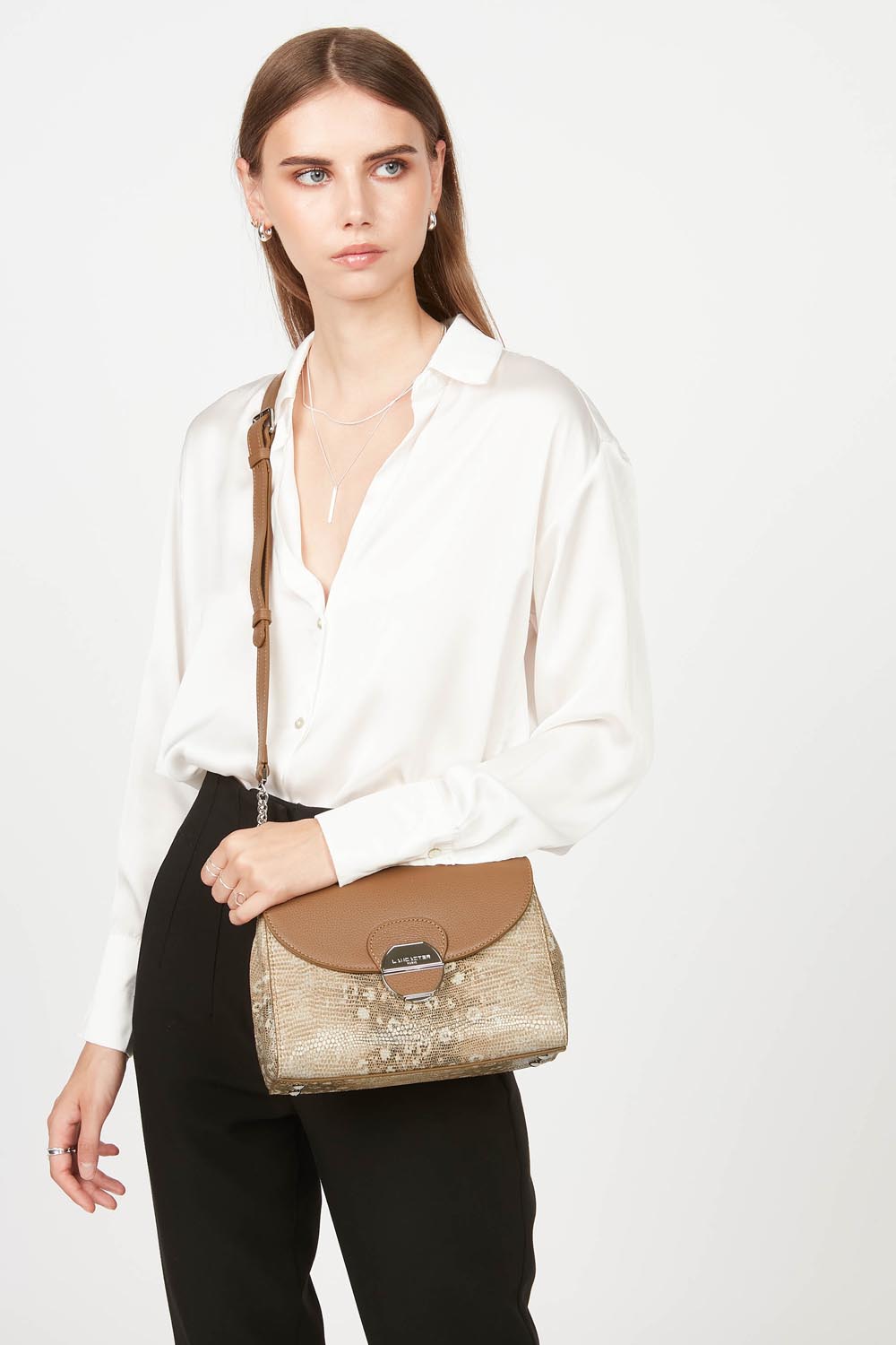Lancaster Pia Camel Flap Crossbody Bag – The Pia trotteur is worn crossbody and pairs with a white shirt and black trousers.