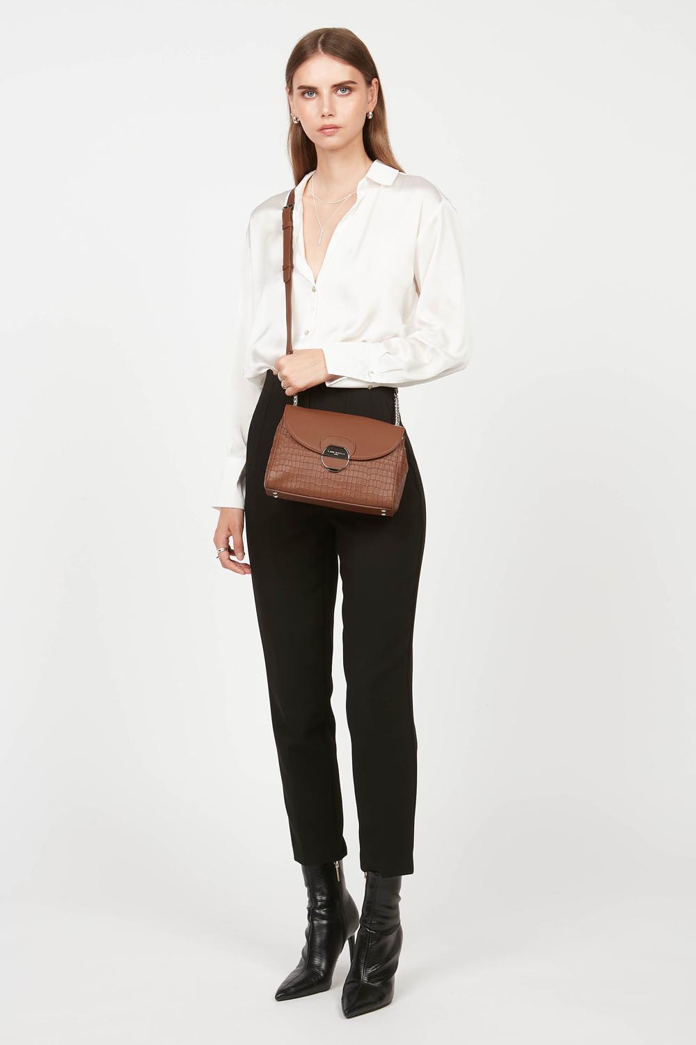 Lancaster Pia Camel Flap Crossbody Bag – Worn crossbody over a white blouse and black trousers, the Pia satchel completes the outfit.