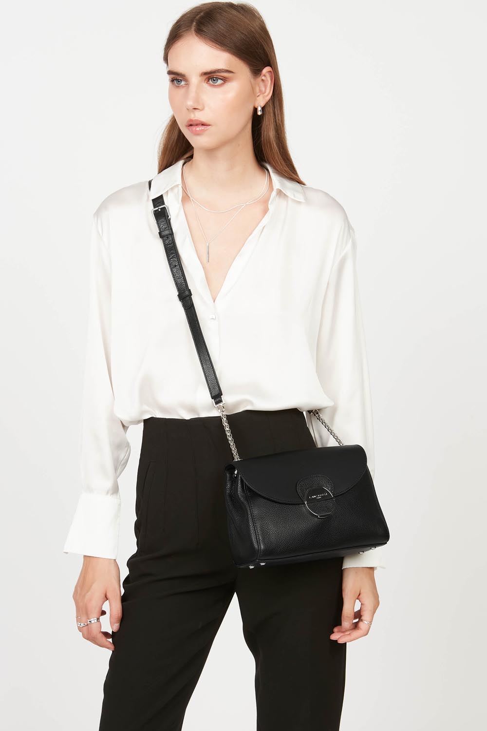 Lancaster Pia Camel Flap Crossbody Bag – The Pia trotteur bag completes a simple look, worn crossbody with a white shirt and black trousers.