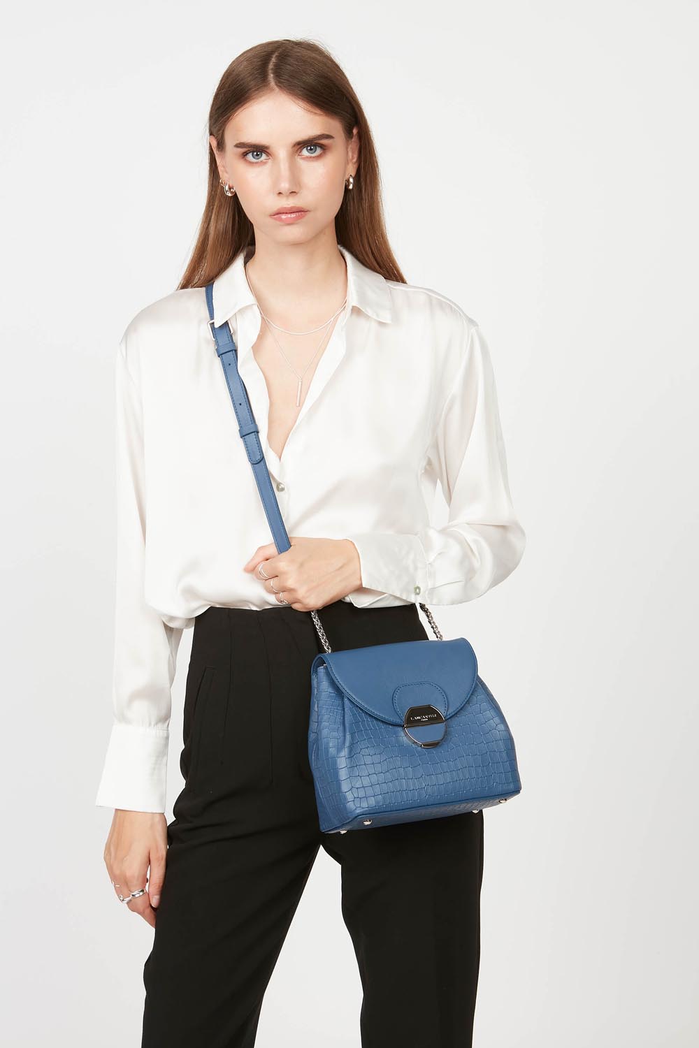 Lancaster Borsa a tracolla con patta e chiusura Pia Camel – Il trotteur Pia blu si porta a tracolla e si abbina a una camicia bianca e pantaloni neri.