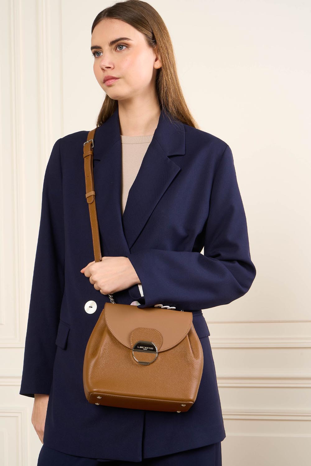 Lancaster Borsa a tracolla con patta e chiusura Pia Camel – La borsa Pia marrone si porta a tracolla con un blazer blu navy e un top beige.