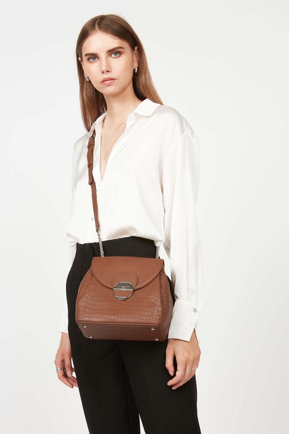 Lancaster Borsa a tracolla con patta e chiusura Pia Camel – Portato a tracolla, il trotteur Pia si abbina a una camicia bianca e a pantaloni neri.