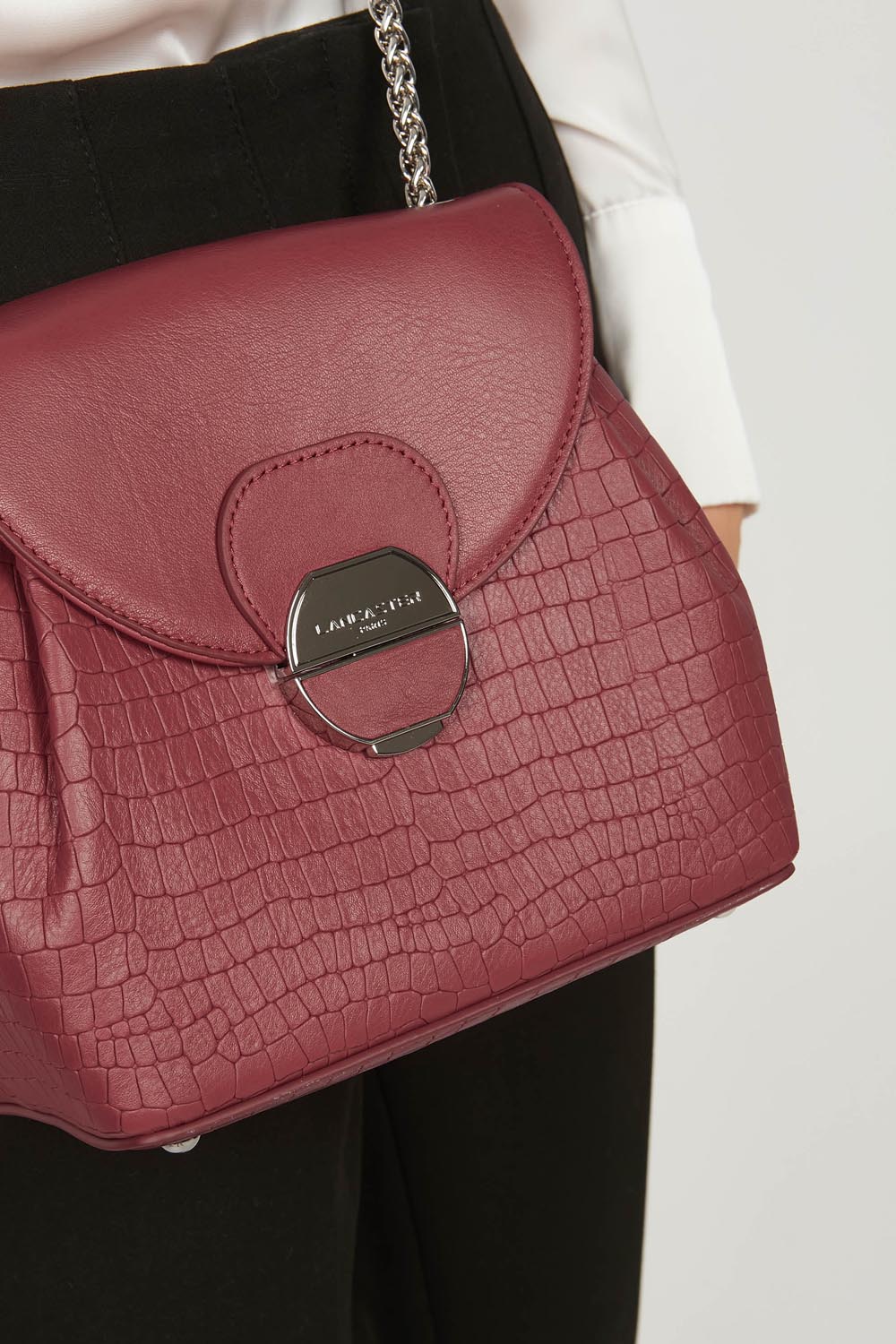 Lancaster Borsa a tracolla con patta e chiusura Pia Camel – A spalla, la borsa trotteur Pia si abbina a una giacca bianca e a pantaloni neri.
