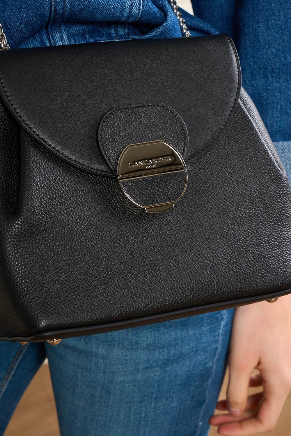 Lancaster Borsa a tracolla con patta e chiusura Pia Camel – La borsa Pia nera è portata a spalla con una giacca di jeans e pantaloni blu.