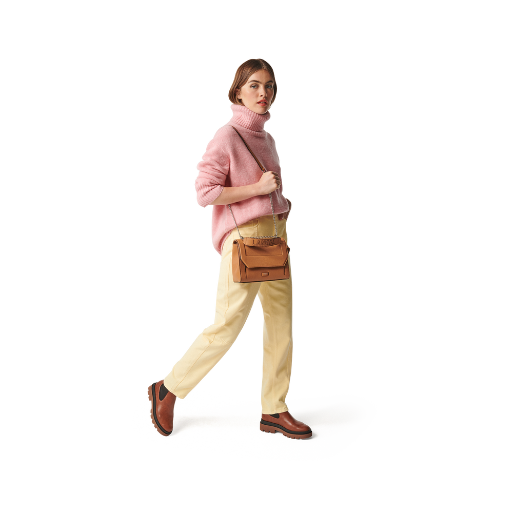 Lancel Ninon brown flap bag, worn over the shoulder with a pink sweater and pale yellow trousers.