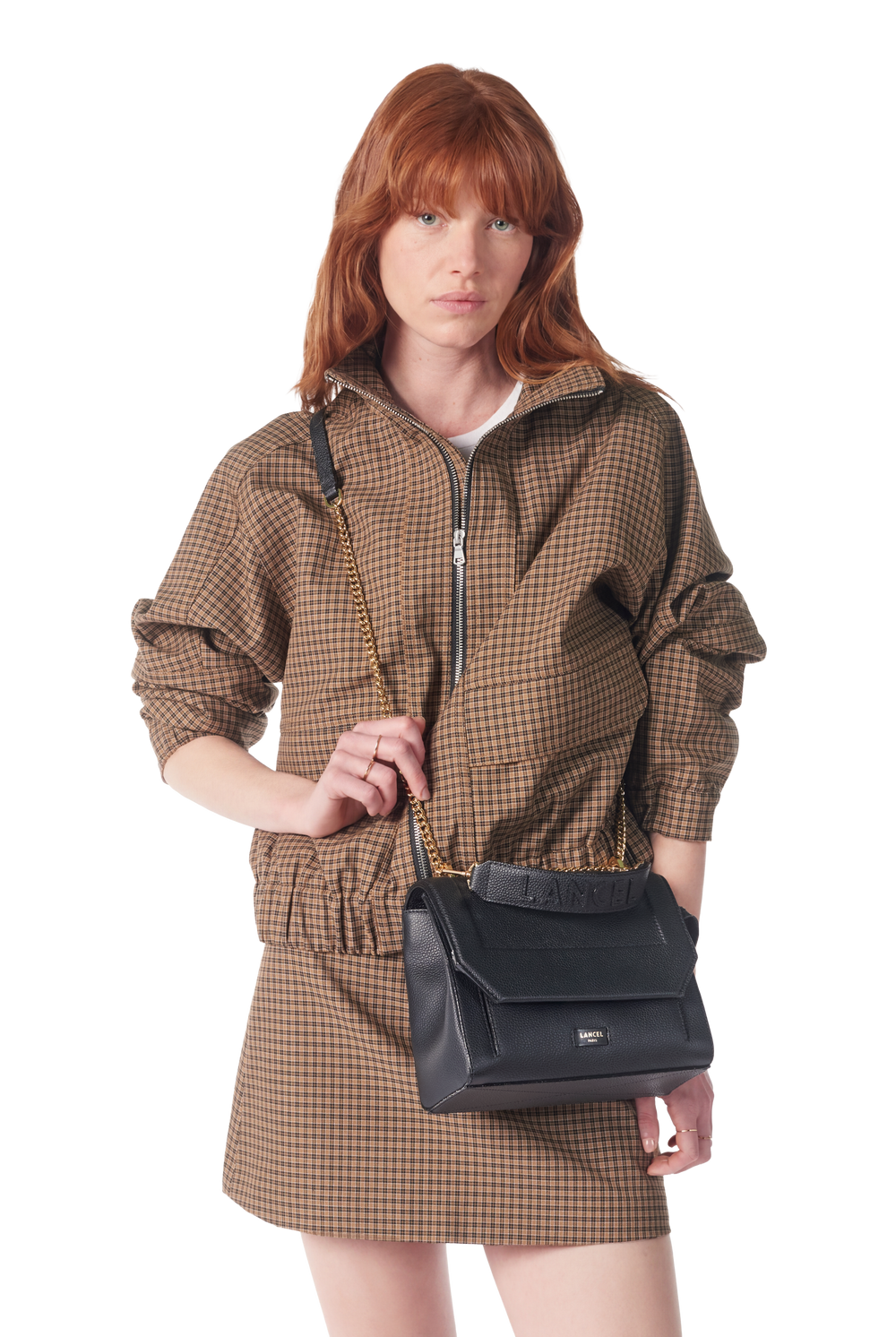 Lancel Ninon black flap bag worn over the shoulder with a brown checked dress.
