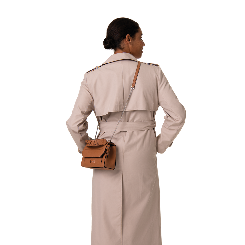Lancel bruine Ninon-tas met klep, schuin gedragen bij een beige trenchcoat.