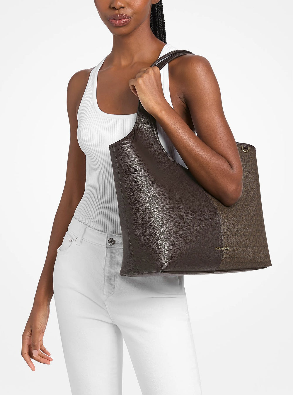 Michael Kors cabas Henly marron porté à l’épaule avec un débardeur blanc et un pantalon blanc.