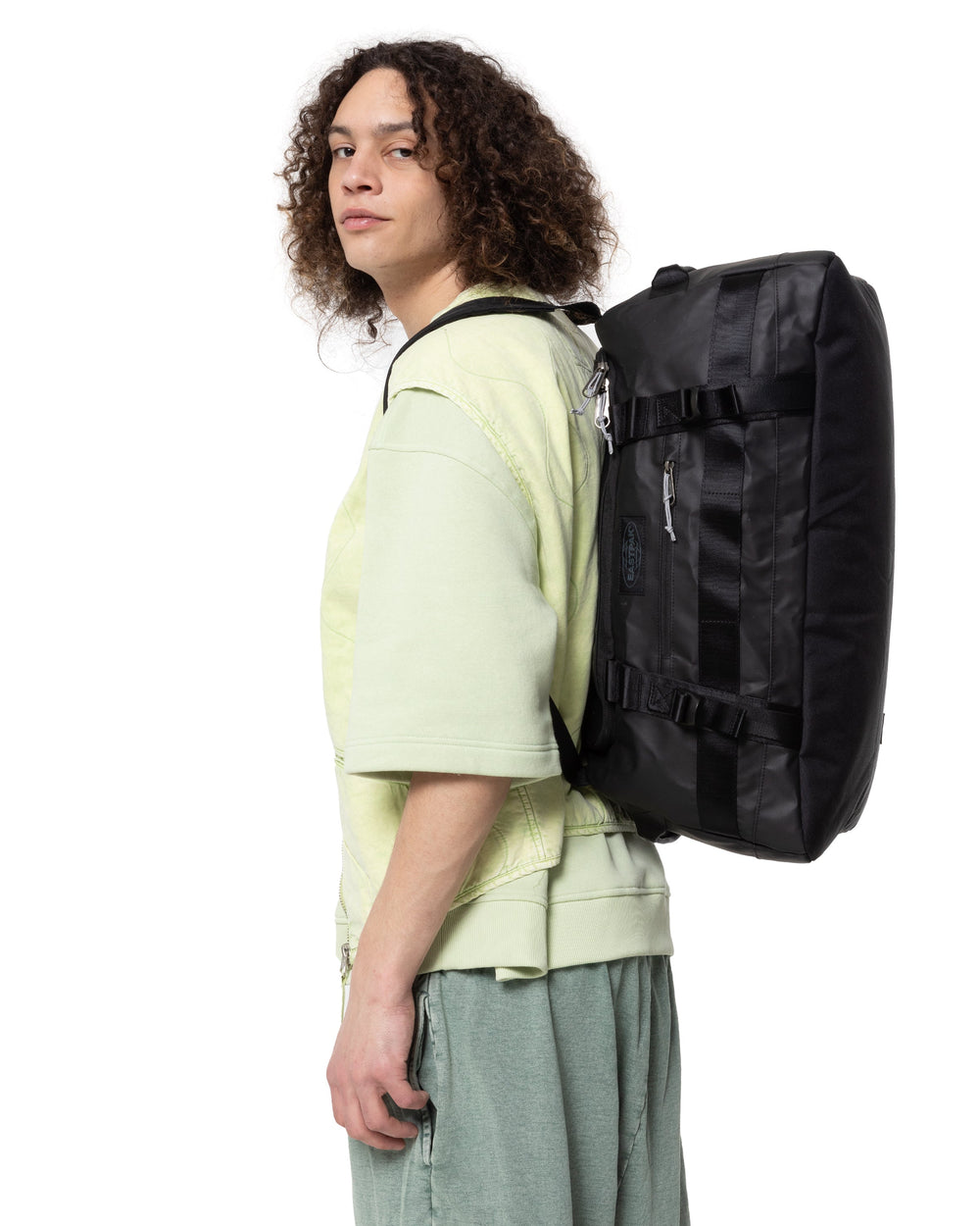 Eastpak sac à dos Duffel Pack S noir porté sur le dos avec un tee-shirt vert pâle et un pantalon gris
