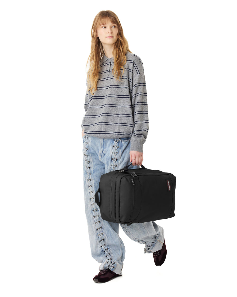 Eastpak czarna torba podróżna Transit’r Pack, niesiona w ręku, z szarym pasiastym swetrem i niebieskimi dżinsami.